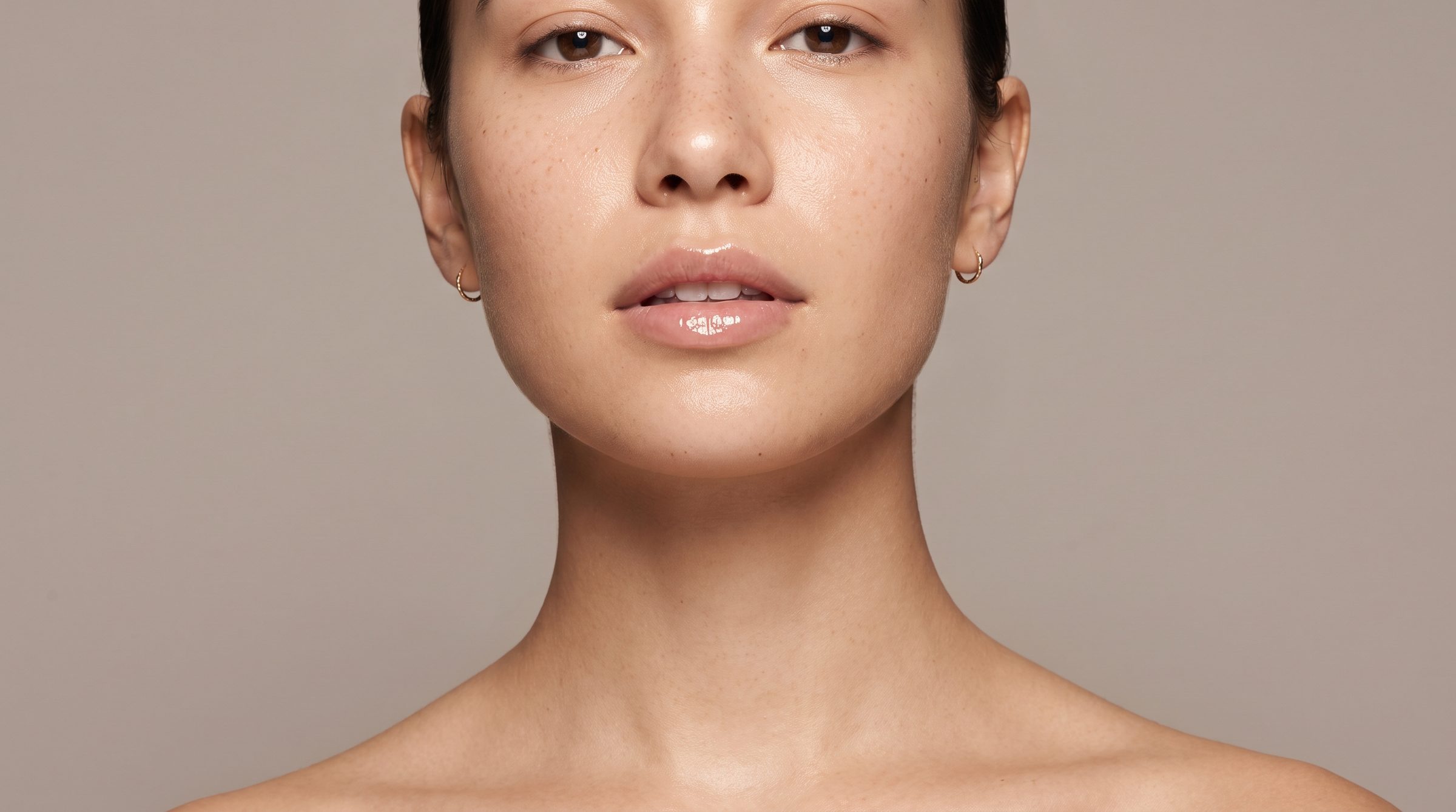 Close-up of a model with luminous, healthy skin against a warm grey backdrop